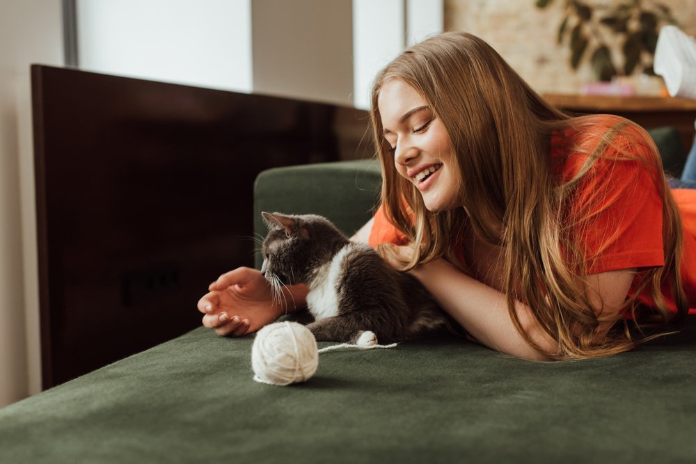 grey and white cat playing with yarn and smiling woman