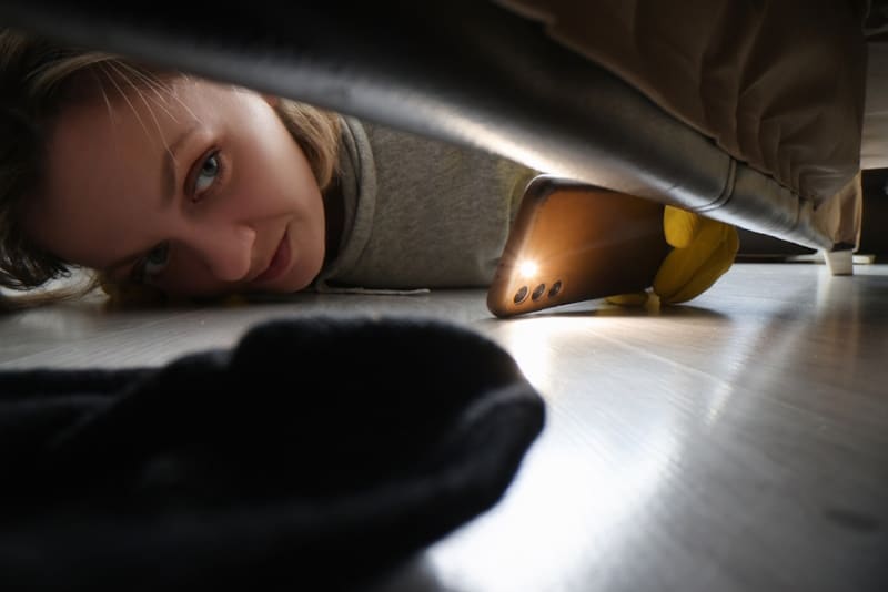 Woman looking for cat under the sofa