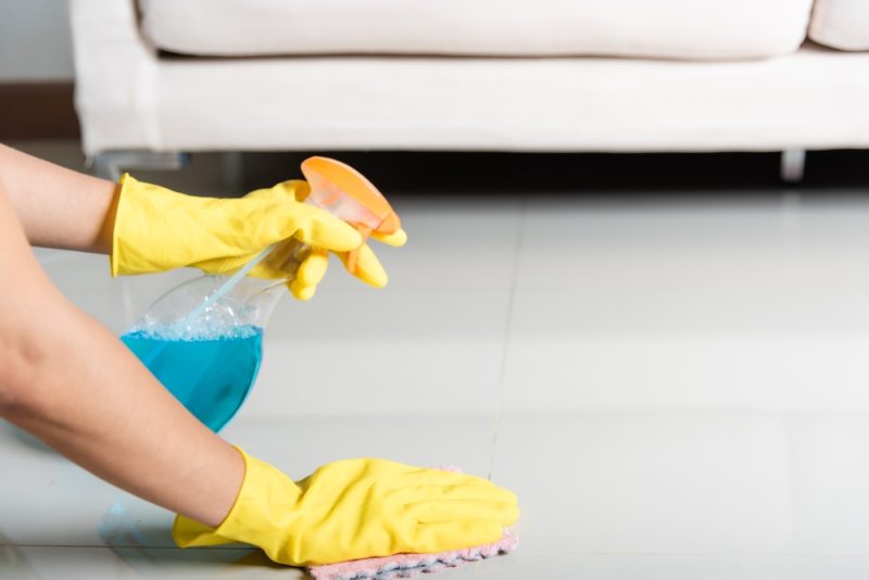 woman wearing rubber gloves spraying the floor